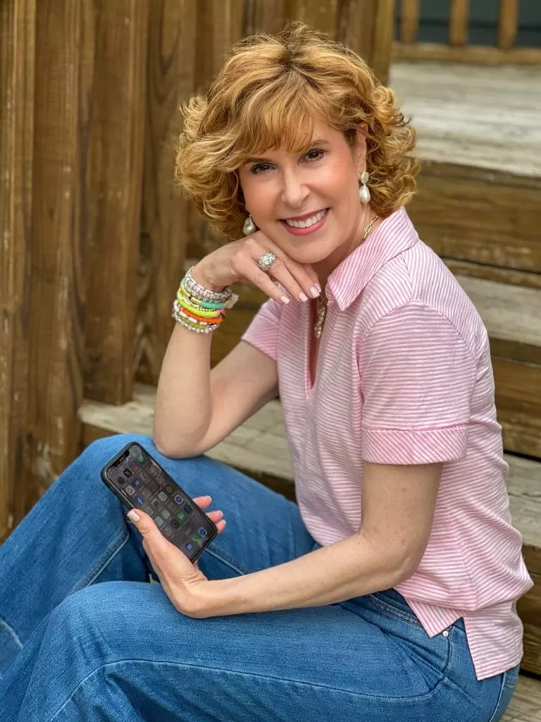 woman wearing pink Talbots Johnny collar shirt holding a smartphone and turning sideways looking at the camera