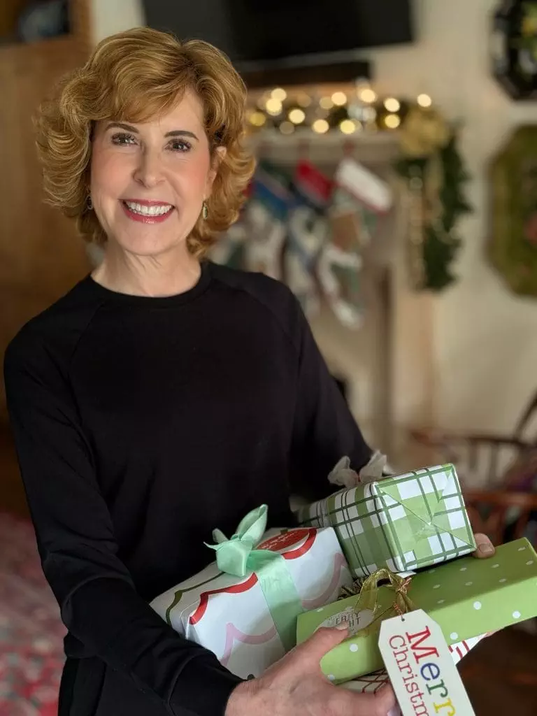 Woman standing in front of a fireplace holding wrapped presents in a black 2 piece jogger set